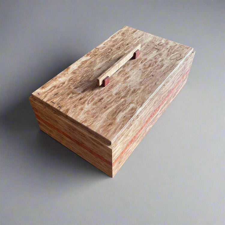 A handcrafted wooden box made of Birdseye Blackbutt timber, with a visible grain pattern and a red handle on the lid.