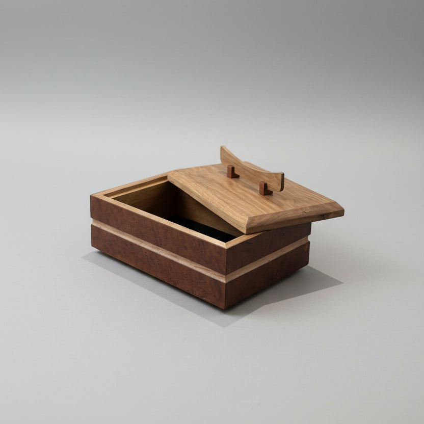 A wooden presentation box with a hinged lid and a small handle, shown open on a wooden countertop in a kitchen or workshop setting.