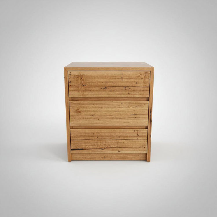A wooden bedside table with three drawers, made from Stringy Bark, with a label indicating the brand 'Wildwood'.